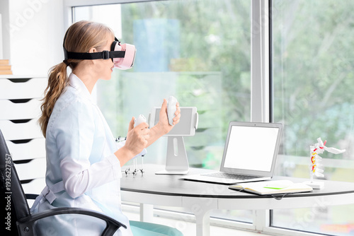 Female doctor using VR glasses with controllers at table in clinic