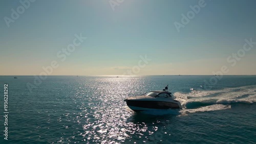 Aerial drone view of a luxury boat cruising across a calm ocean in Miami, Florida with sunlight reflecting on the sea.