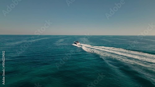 Aerial drone view of a luxury boat cruising across a calm ocean in Miami, Florida leaving a white wake trail.