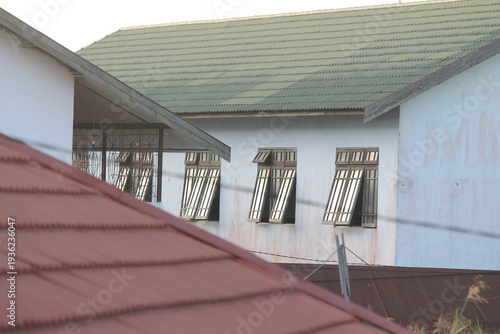 Row of open wooden windows on a white building wall with a green corrugated roof. The composition shows typical institutional or school architecture in a tropical region. Useful for education and trav