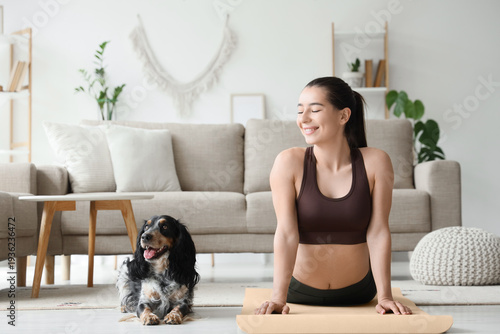 Sporty young woman with cute dog doing yoga at home