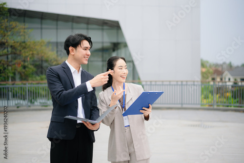 Asian business professionals discussing documents outdoors, showcasing teamwork, corporate strategy, leadership and modern workplace collaboration