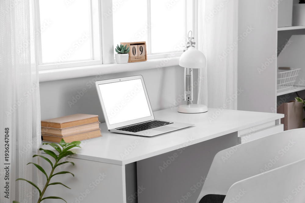 Fototapeta premium Blank laptop with books and lamp on desk in office