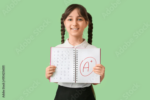 Happy schoolgirl holding notebook with good results of school test on green b...