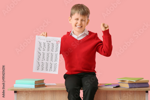 Happy schoolboy with books and good results of school test sitting on desk ag...