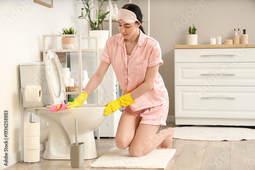 Young woman cleaning toilet...