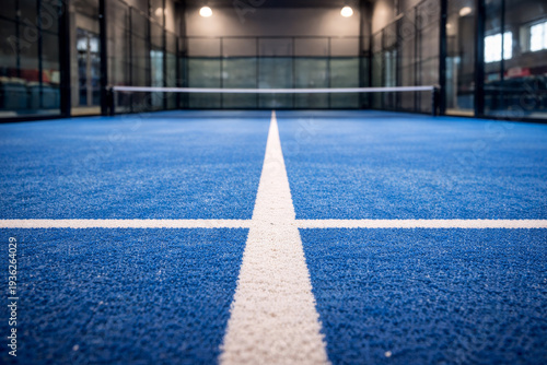 Low angle perspective of blue padel court surface with white lines and net inside modern indoor sports facility.