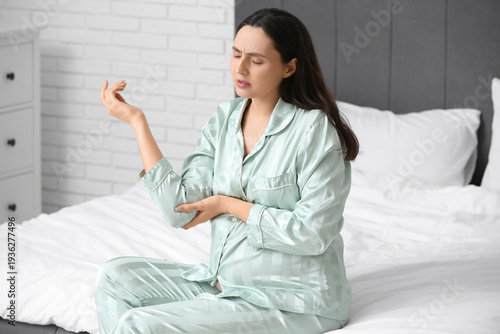 Tableau sur toile Pregnant young woman in pajamas suffering from pain in elbow on bed at home