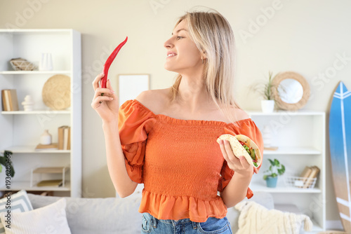 Young woman with tasty taco and hot chili pepper at home