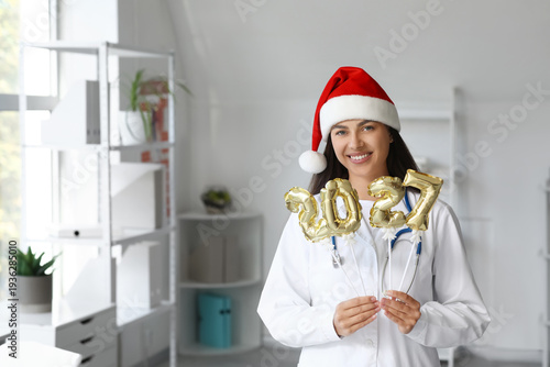 Young female doctor with Santa hat and balloons in shape of figure 2026 in cl...