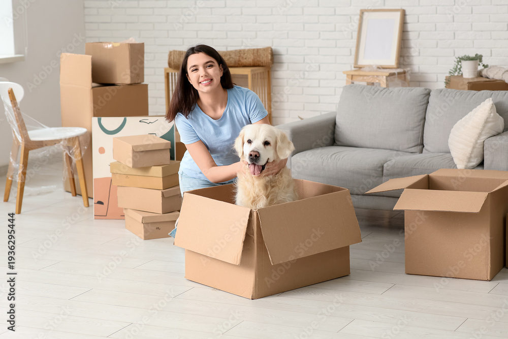 Fototapeta premium Young happy woman and cute Labrador dog with boxes on moving day sitting at home