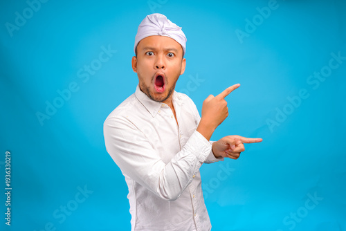 Surprised Balinese man wearing traditional udeng pointing up to the copy space beside him.