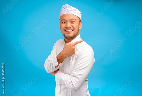 Happy Balinese man wearing Indonesian traditional udeng pointing to the copy space on behind him.
