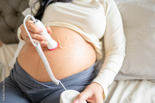 Pregnant Woman Using Fetal Doppler to Listen to Baby Heartbeat at Home