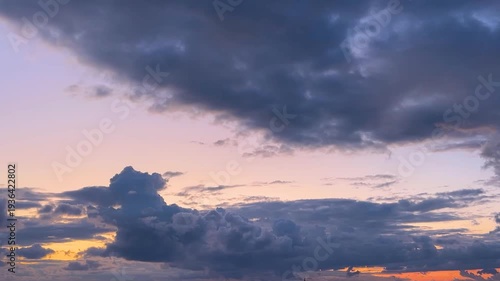 Dark, stormy clouds rolling across a colorful sunset sky as day turns into night