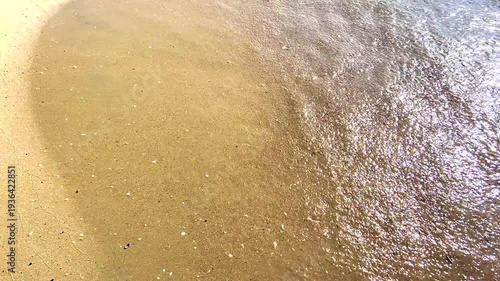 Calm sea waves gently washing over a beautiful golden sandy beach on a sunny summer day