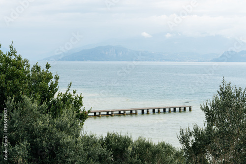 Wallpaper Mural Pier extending into Lake Garda with mountains in the background under a cloudy sky. Torontodigital.ca
