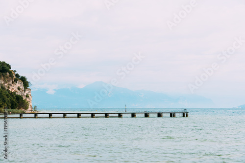 Wallpaper Mural Pier extending into Lake Garda with mountains in the background under a cloudy sky. Torontodigital.ca