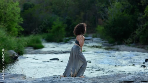 A Serene Moment by the River: Captivating Female Figure in Flowing Attire Creates a Connection with Nature While Standing Amidst Lush Greenery and Calm Waters