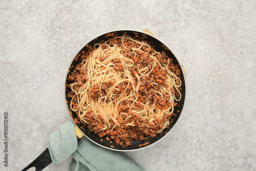 Cooked pasta with meat sauce in a large frying pan on a light surface during a meal preparation