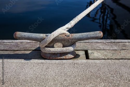 Close-up of a dock cleat with rope securely tied, taken at Charleston Marina in Oregon. The weathered textures of the metal and wood add a maritime feel to this nautical detail scene.