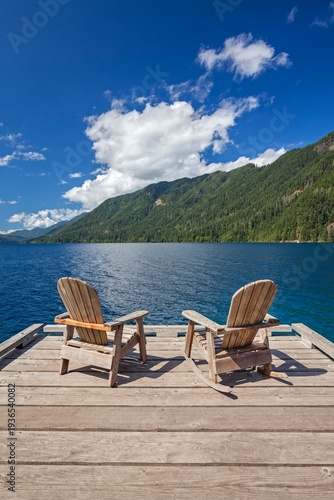 Two Adirondack chairs rest on a wooden dock with views of Lake Crescent and surrounding mountains in Olympic National Park, Washington.