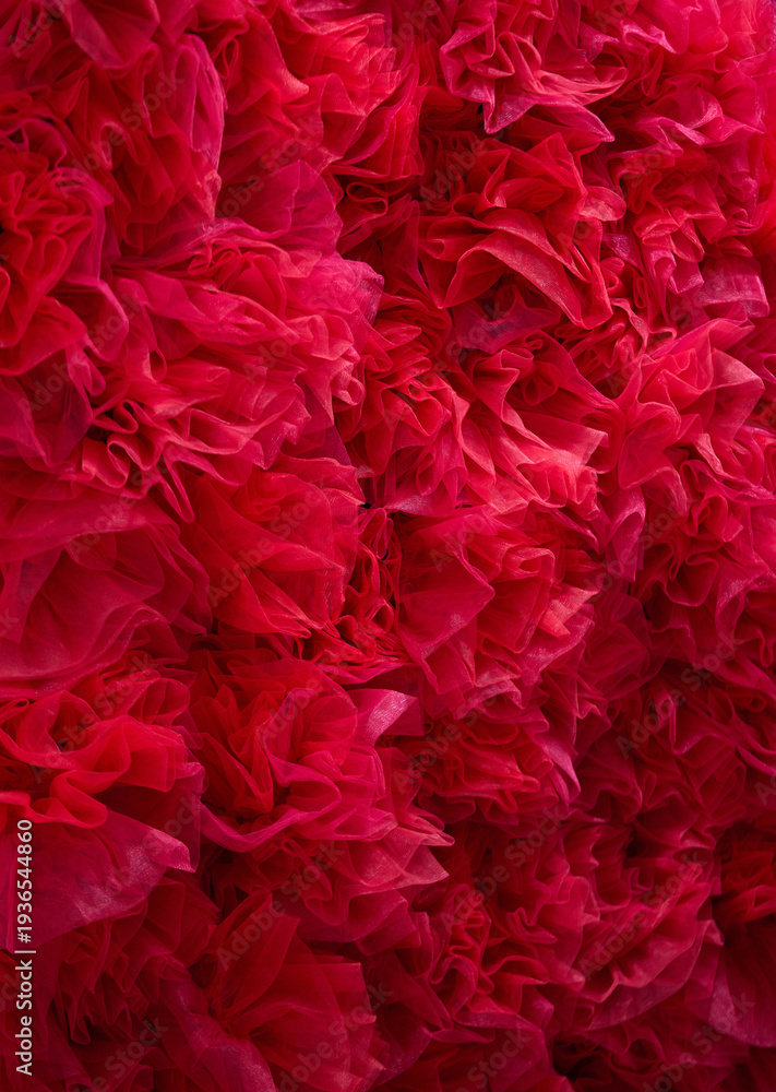 Fototapeta premium Vibrant red tulle fabric texture. A dense arrangement of ruffled and layered soft mesh material, creating a voluminous and romantic abstract background for fashion or floral concepts.