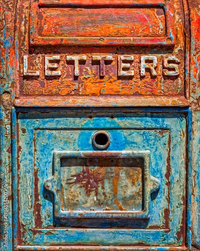 Close up of an antique metal mailbox with peeling turquoise and orange paint and the word LETTERS in relief, showing rust, patina, texture, and bold color for a grunge background.