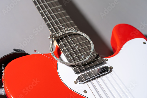 Close-up of a red electric guitar with white pickguard, chrome hardware, dual pickups, bridge saddles, and a coiled set of new metallic strings resting on the body.