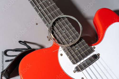 Close-up of a red electric guitar with white pickguard, dark fretboard, metal frets, dot inlays, and a coiled set of new metallic strings resting across the neck and body.