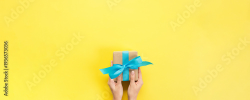 Wallpaper Mural Woman arms holding gift box with blue ribbon on color background, top view Torontodigital.ca