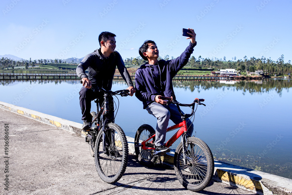 Fototapeta premium Cyclists Taking Break To Snap Selfie And Rest Beside Tranquil Lake