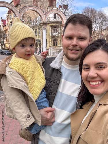 Happy family selfie in park with toddler wearing yellow beanie Portrait