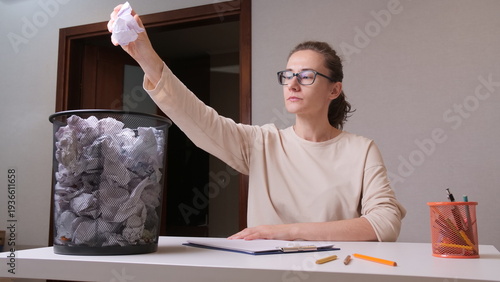 Foto Woman wearing glasses at a white desk throws crumpled paper into an overflowing