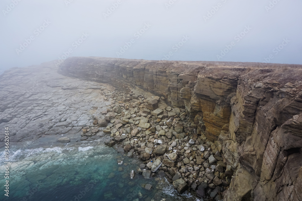 Obraz premium The rocky and foggy coastline of Russky Island
