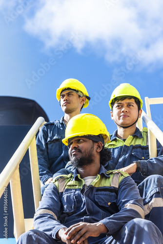 Maritime workers relaxing briefly during work shift on the outer staircase of a merchant ship superstructure.