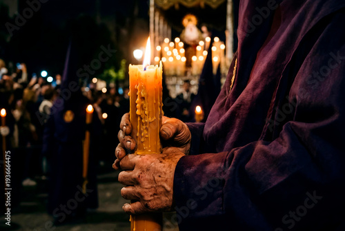 Close-up of hands holding a large burning candle during a Semana Santa procession in Spain. A traditional robe sleeve is visible while warm candlelight illuminates melting wax
