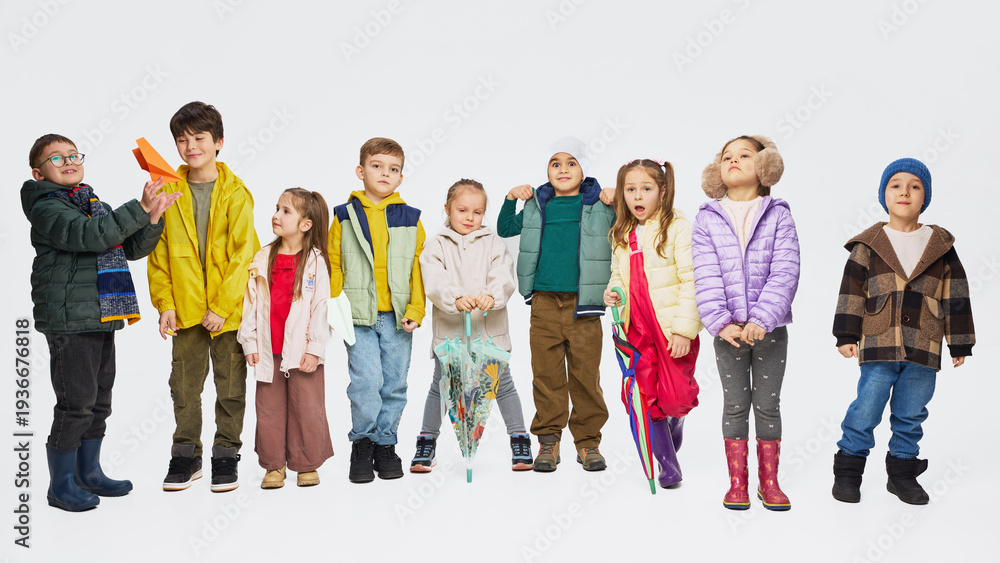 Fototapeta premium Group of children wearing colorful autumn outfits standing together in studio. Concept of kids fashion collection, seasonal clothing styles, playful childhood and modern children apparel.