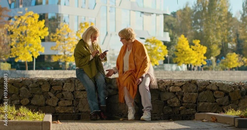 Senior women friends chatting and using a smartphone in a city park