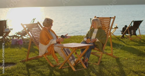 Senior women friends enjoying a conversation by the lake at sunset