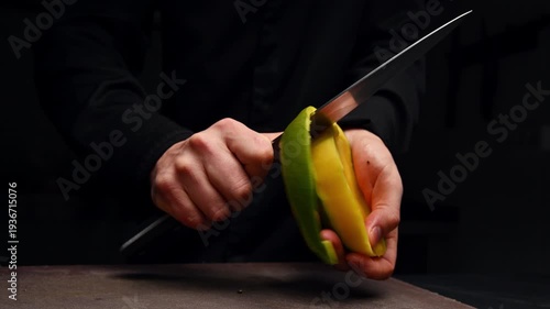 Chef peels mango with knife, showcasing continuous slicing action in kitchen