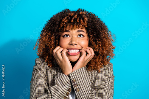 Картината върху платно Young woman with curly hair in a checkered blazer smiles anxiously against a bri