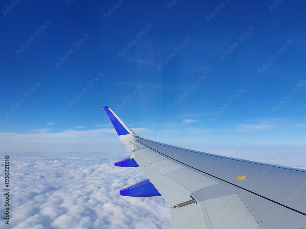 Obraz premium Phone photo of a blue sky over clouds with an airplane wing in view. Aerial travel scene showing altitude, flight perspective, and serene cloudscape.