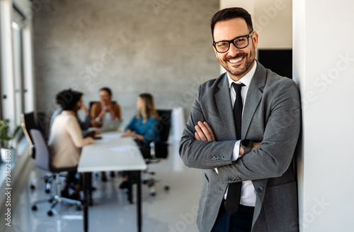 Handsome young business man standing confident in the corporate office in front of his team