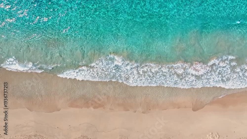 Aerial view of a sandy sea beach background. Looping ocean texture, aerial view of calmly moving ocean waves. Flying over a sandy beach and waves, seamless loop of a sunset beach.