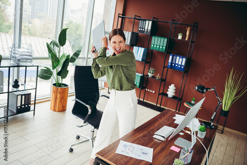 Fotografija Frustrated office worker raising clipboard in anger at desk in modern workplace,