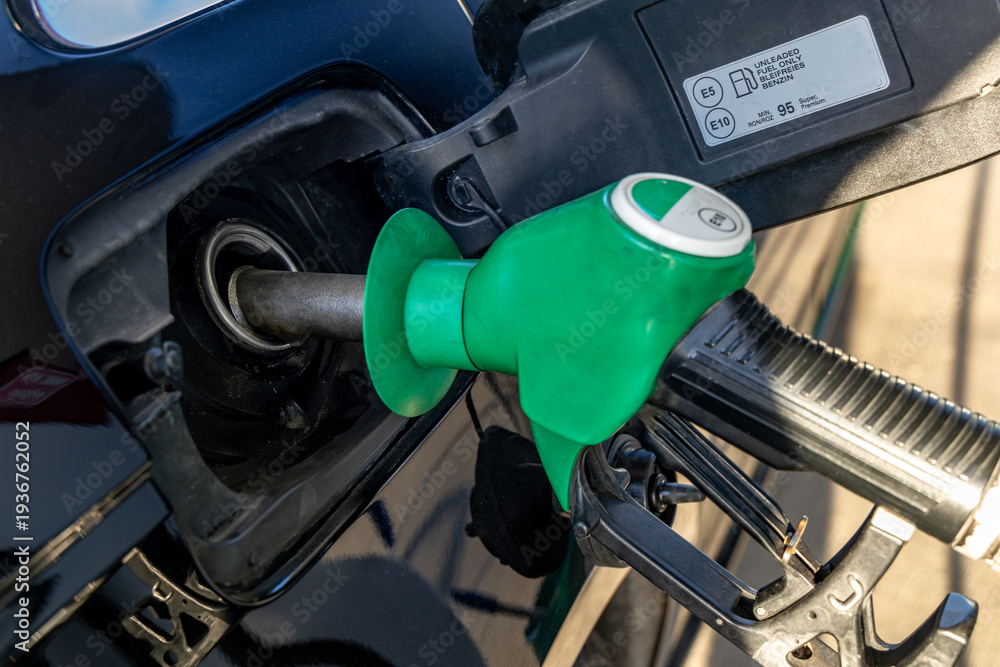Fototapeta premium Green fuel dispenser inserted into the fuel filler of a car, filling up a car, rising fuel prices in the world