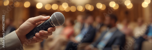 Close-up of a hand holding a microphone against the background of blurred people in a conference room