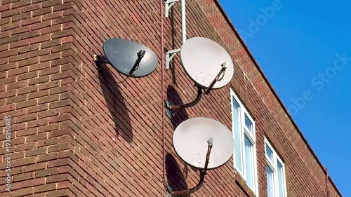 satellite broadcast dishes antenna on side of brick building with blue sky