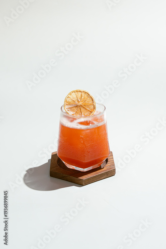 Refreshing Orange Drink with Dehydrated Citrus Garnish on Wooden Coaster.